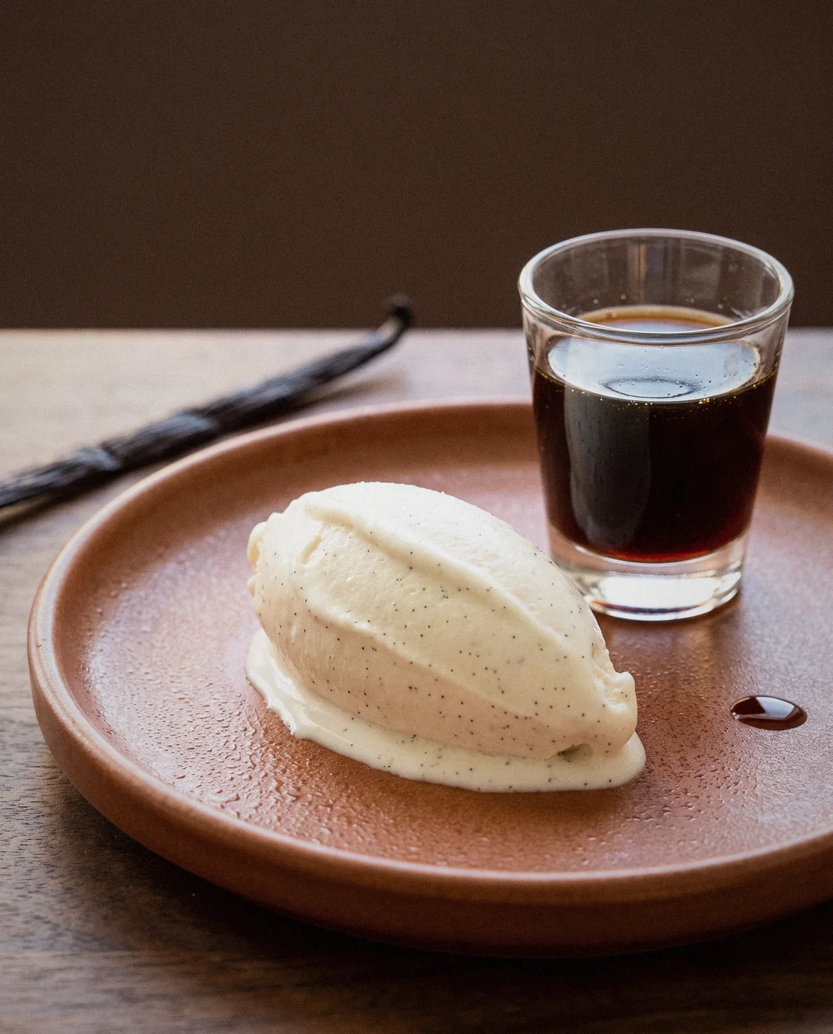 Scoop of vanilla ice cream on a terracotta plate beside a small glass of vanilla extract Scoop of vanilla ice cream on a terracotta plate beside a small glass of vanilla extract