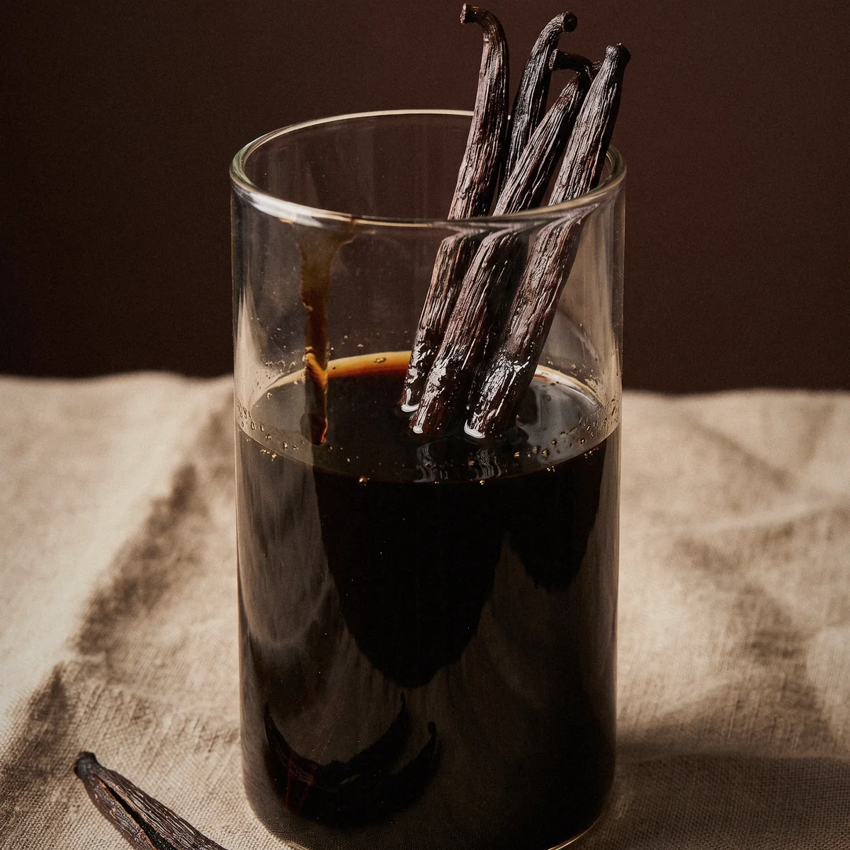 Vanilla beans macerating in a glass of dark extract, on linen