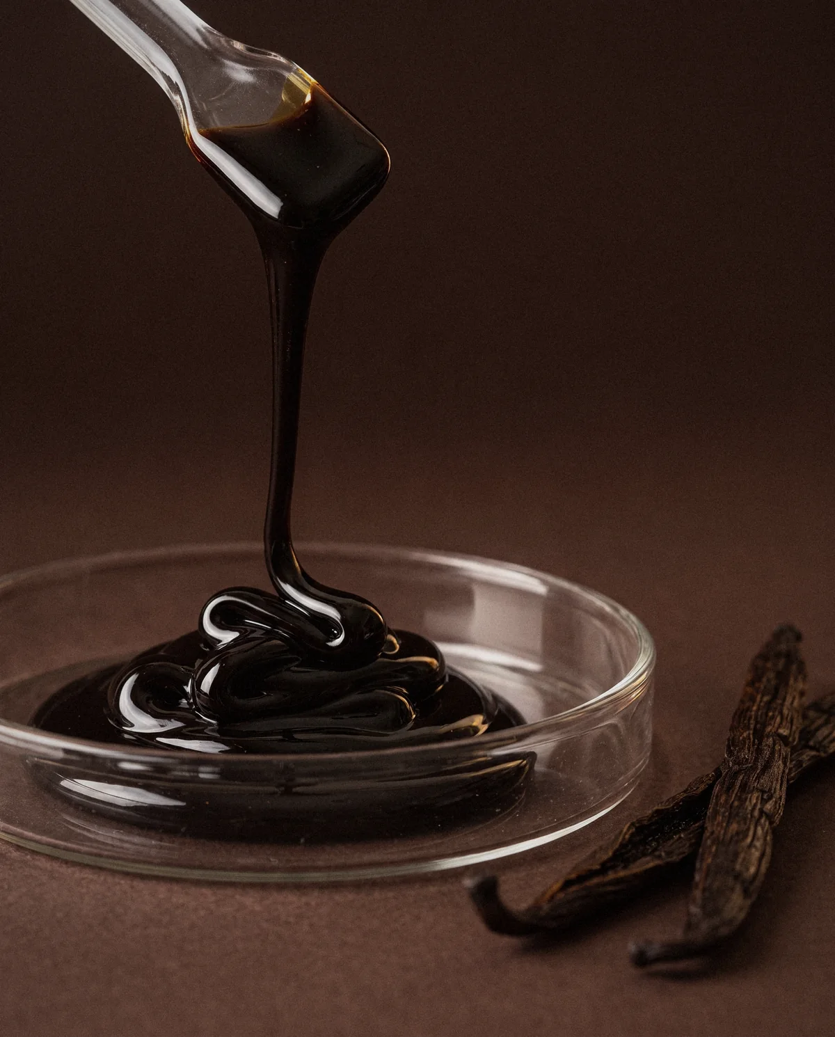 Ruban épais d'oléorésine de vanille coulant d'une spatule en verre dans une coupelle en verre Ruban épais d'oléorésine de vanille coulant d'une spatule en verre dans une coupelle en verre