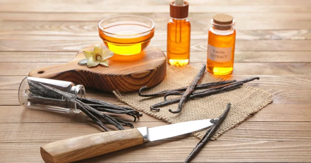 An arrangement of vanilla beans, a honey jar, vanilla extract bottles, and a carving knife on a rustic wooden surface, illustrating the process of making vanilla extract.